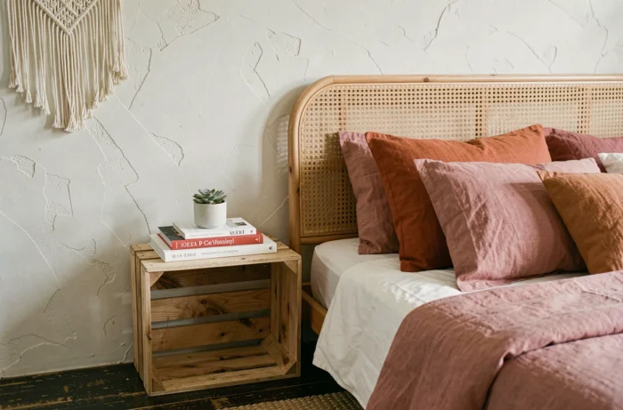 Esquina de habitación bohemia moderna con cabecera de ratán, almohadas de lino terracota y caja de madera reciclada como mesita de noche