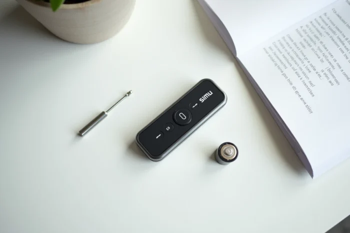 Télécommande Simu posée sur une table avec tournevis, pile et notice pour une procédure de réinitialisation